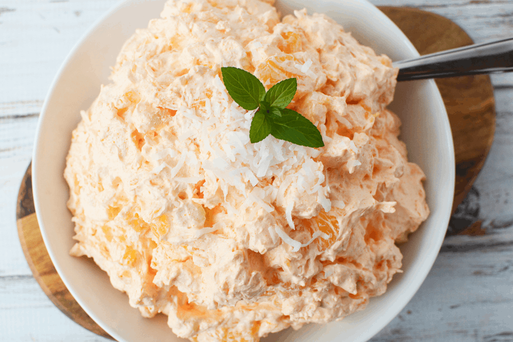 Orange JELLO Salad filled with mini marshmallows, pineapple, shredded coconut in a bowl